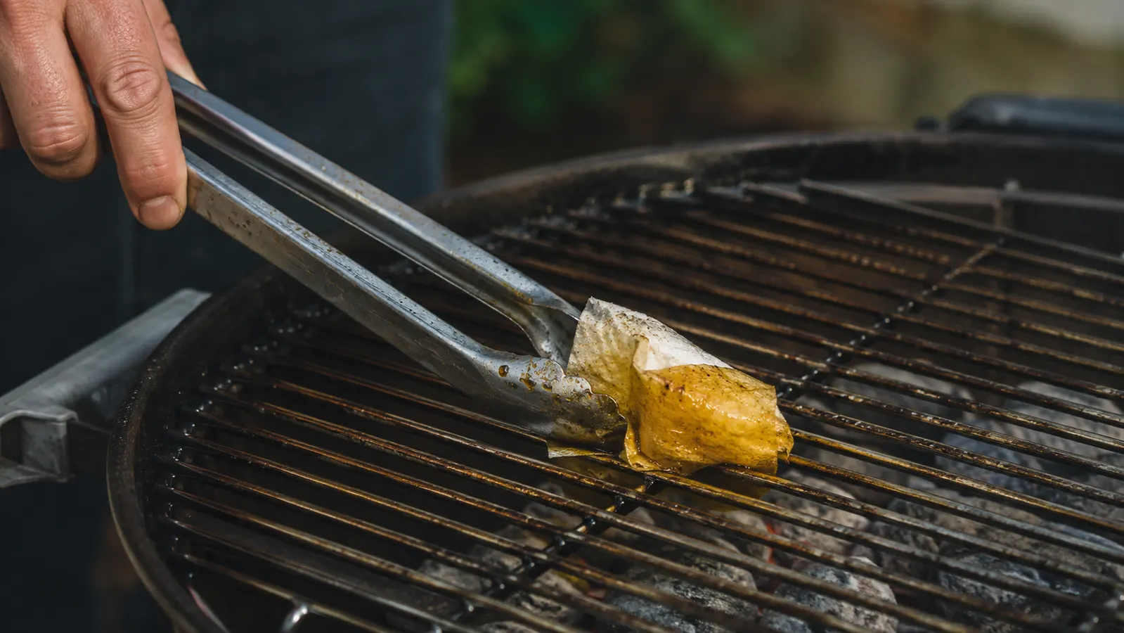 Grill grates being lightly oiled with a folded paper towel held by tongs before cooking